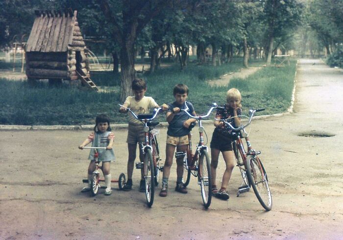 Four children with bicycles in a park, capturing a hilarious and awkward childhood moment outdoors.