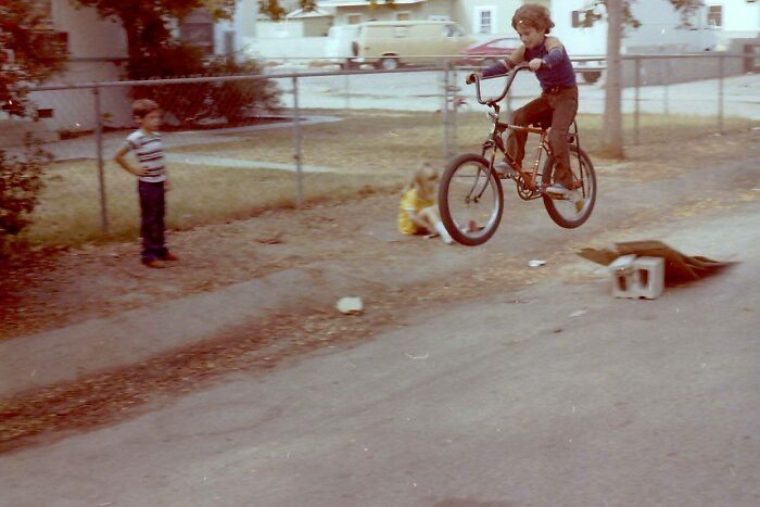 Childhood photo of a boy performing a bike jump stunt while another child watches, capturing an awkward moment.