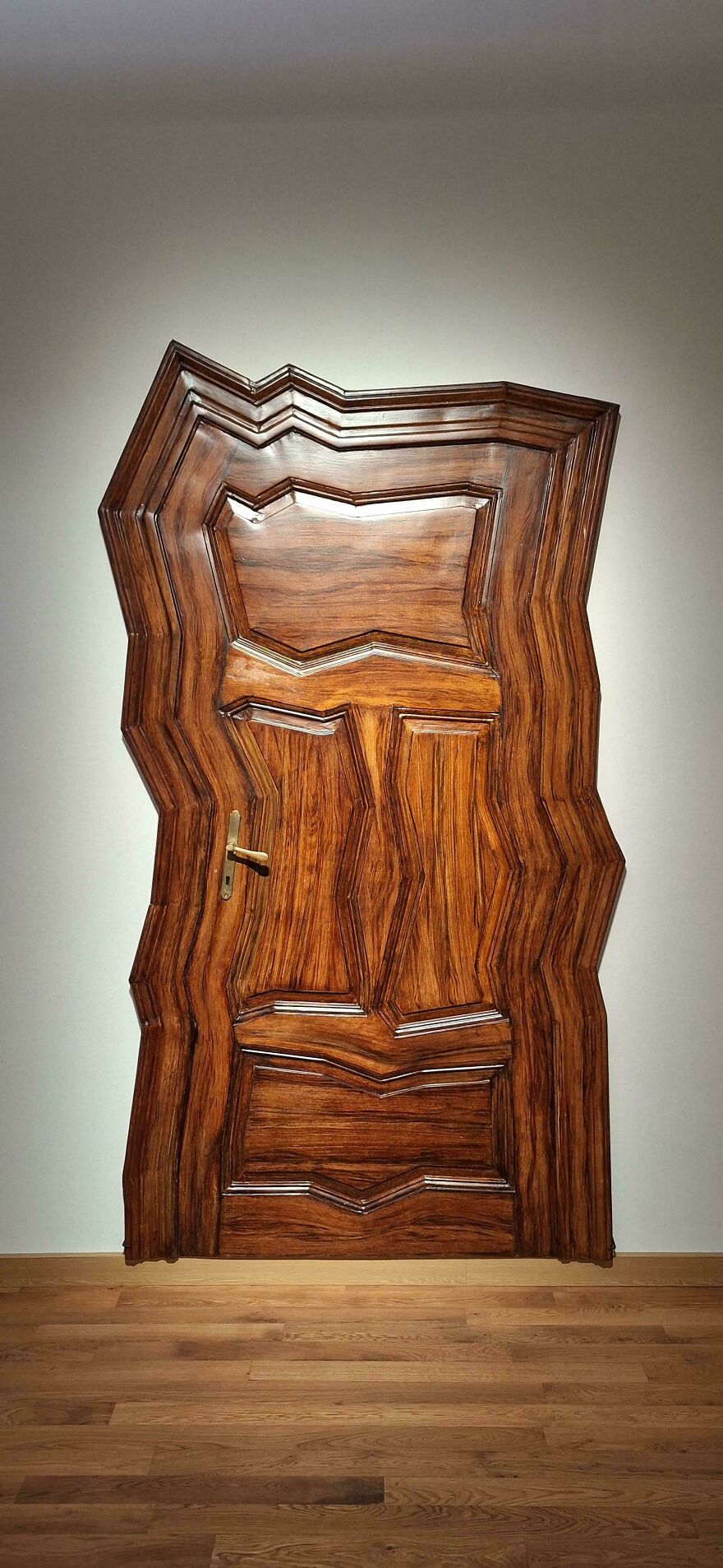Distorted wooden door with irregular zigzag edges, creating a weird and unexplainable visual experience indoors.