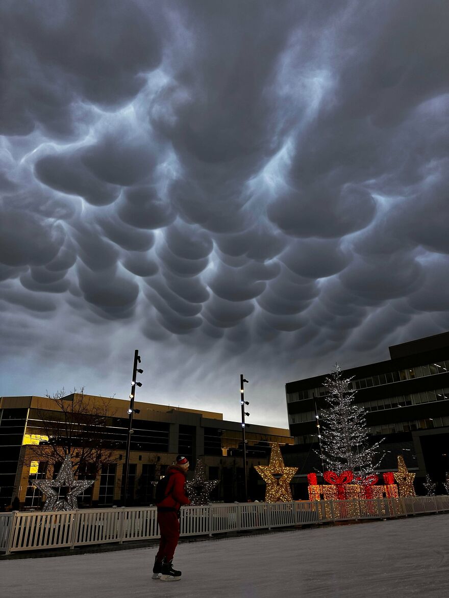 Unexplainable mammatus clouds forming above a decorated outdoor ice skating rink at dusk.