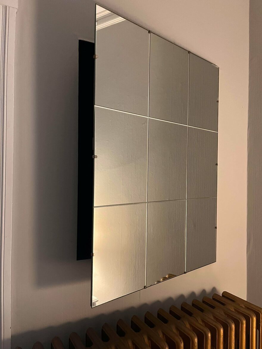 Wall mirror made of nine separate tiles mounted above a wooden radiator in a room, showing a weird unexplainable reflection.