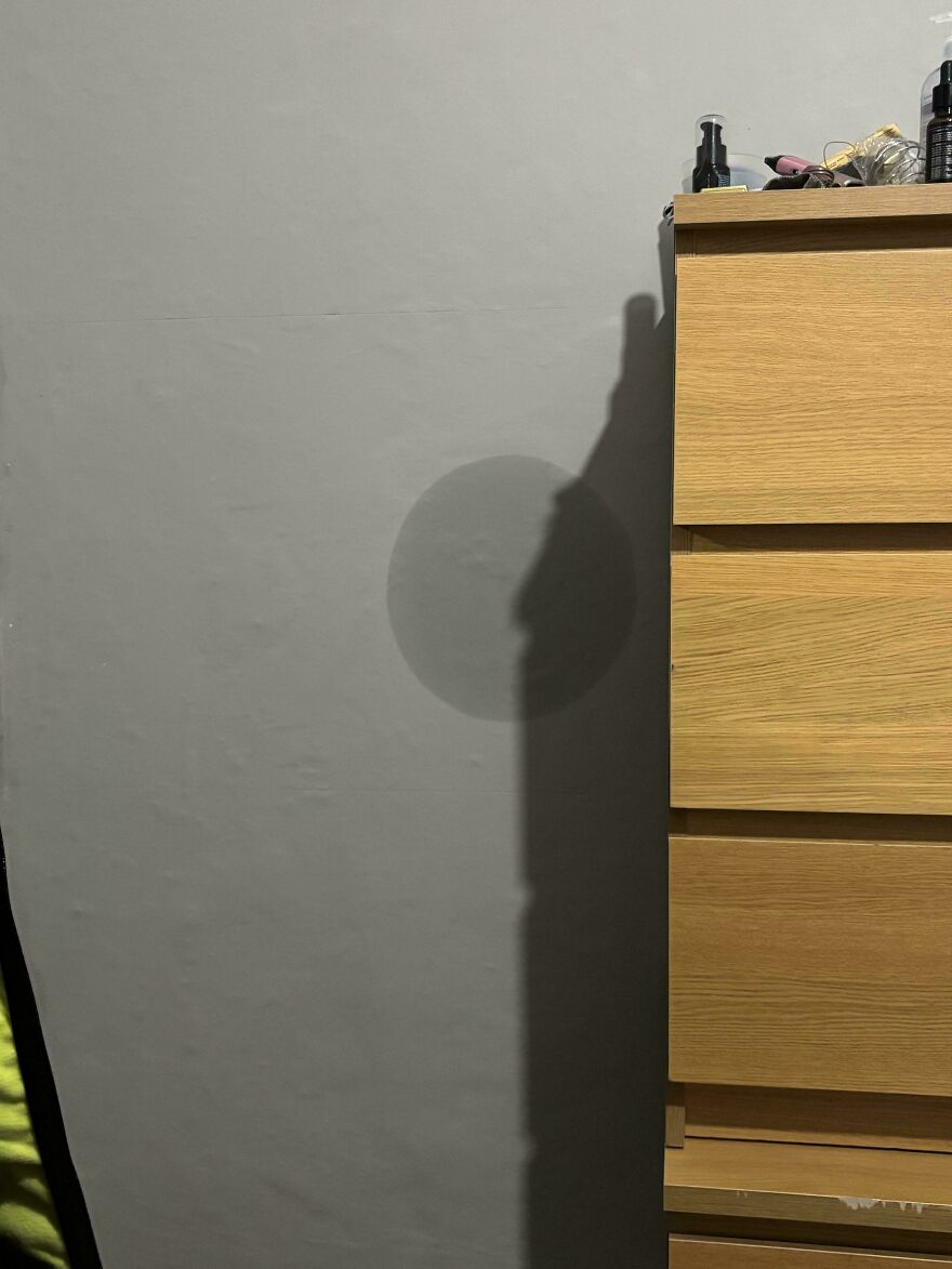 Shadow on wall resembling a human face beside a wooden dresser, a weird and unexplainable thing experienced by people.