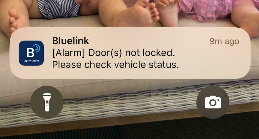 Notification on phone screen showing vehicle door unlock alert, surrounded by children's feet on a couch in a weird and unexplainable setting.