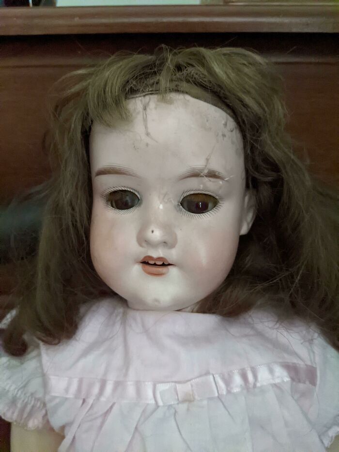 Vintage creepy doll with cracked face and disheveled hair found in an old home, evoking bizarre and eerie vibes.