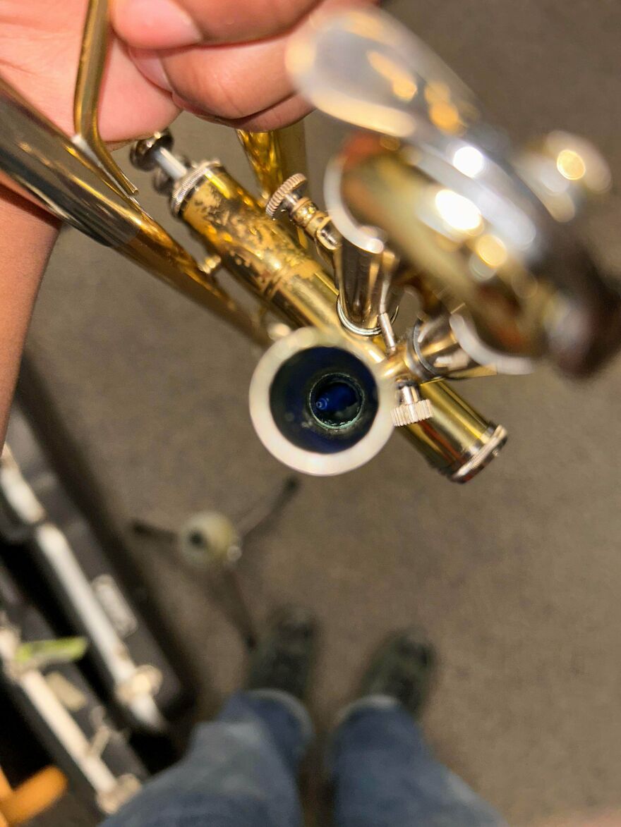 Close-up of a person's hand holding a trumpet with a mysterious blue object inside the bell in a carpeted room.