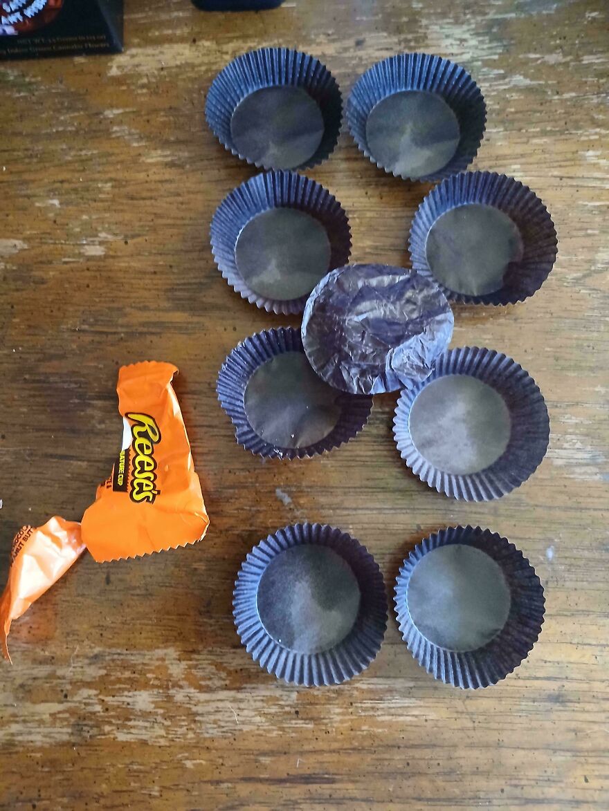 Empty Reese's peanut butter cup liners arranged neatly with an empty candy wrapper on a wooden table, weird and unexplainable.