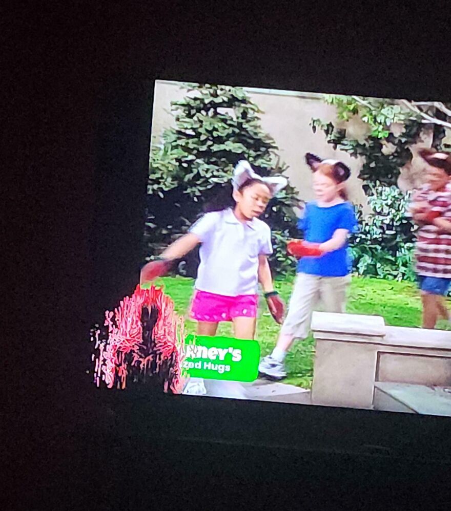 A weird and unexplainable shadowy figure appears on the screen behind children playing outside.