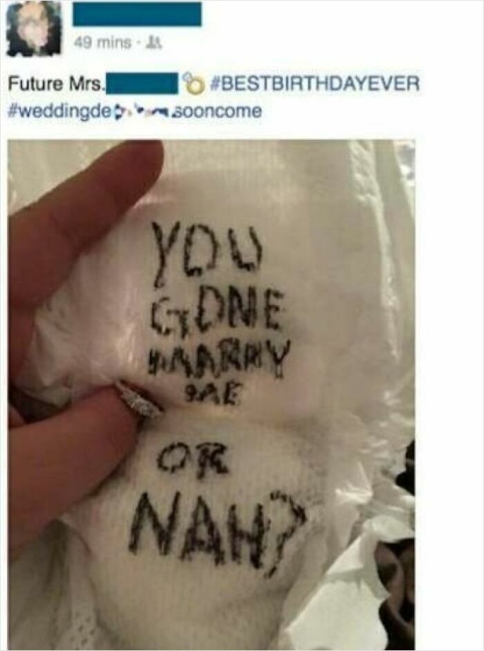 Hand holding a napkin with a cringeworthy marriage proposal message written in ink, featuring an engagement ring.