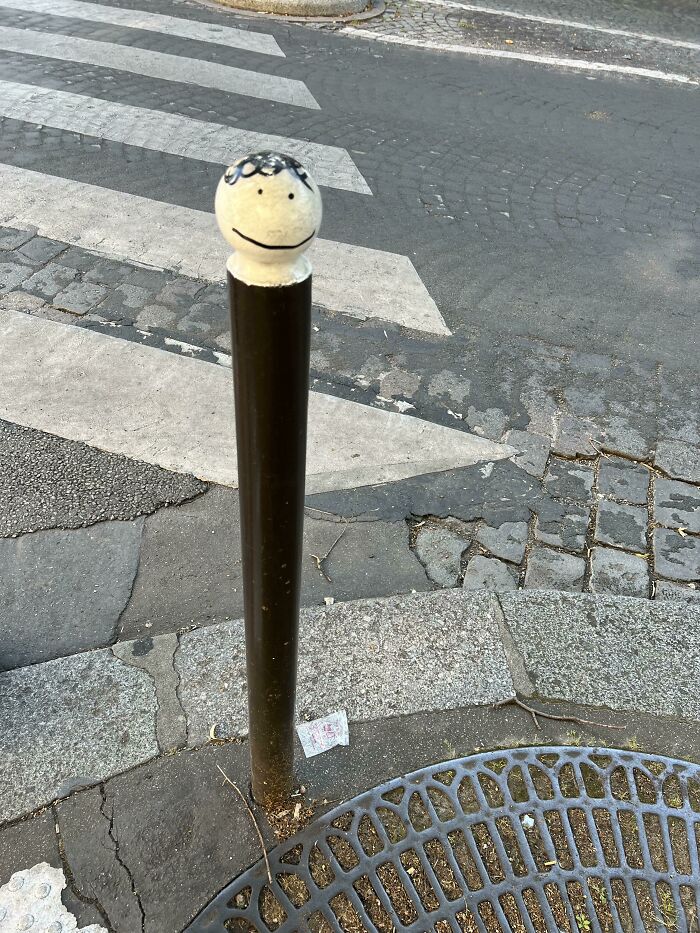 Smiley face drawn on a street bollard, an example of mild vandalism adding humor to urban surroundings.