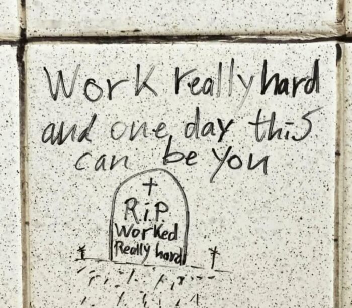 Handwritten graffiti on a wall humorously warning about working really hard with relatable memes theme.