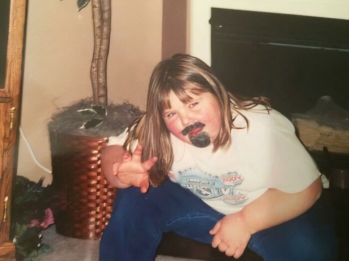 Child with drawn-on beard and mustache posing awkwardly in a living room, a hilariously awkward childhood pic.