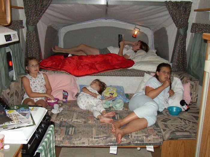 Three kids in pajamas lounging awkwardly inside a camper, sharing a snack and looking unimpressed in childhood pics.