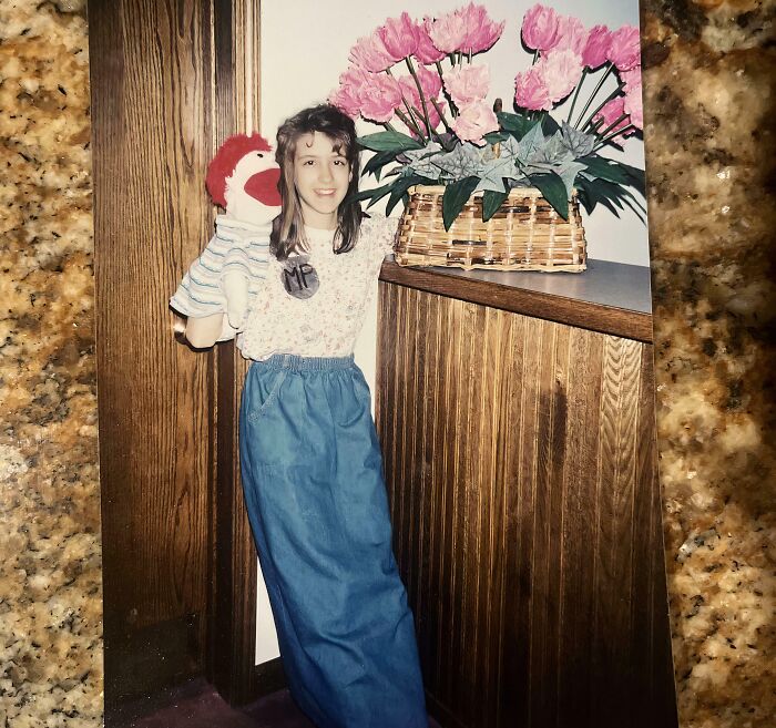 Young girl holding a sock puppet and wearing a long denim skirt in a vintage awkward childhood photo.
