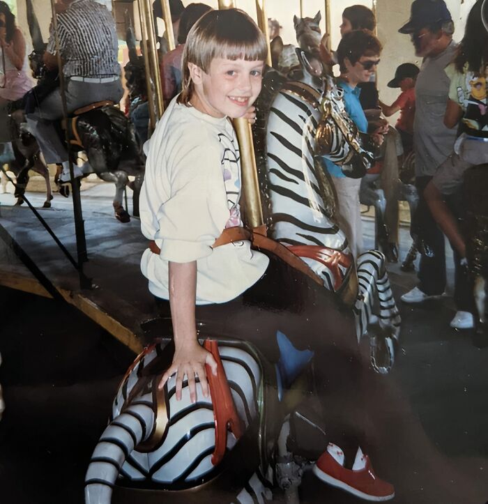 Child on a striped carousel ride smiling awkwardly, a funny and awkward childhood picture shared by people.
