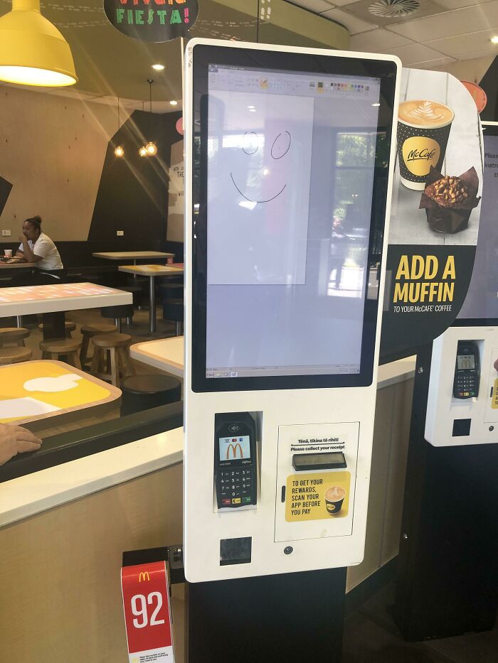 Self-order kiosk at a fast food restaurant with mild vandalism showing a smiley face drawn on the screen.