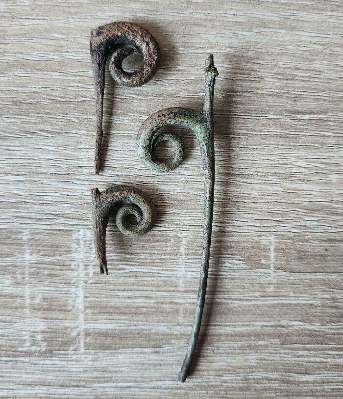 Three rusted metal sticks with spiral ends laid out on a wooden surface representing cool sticks collection.