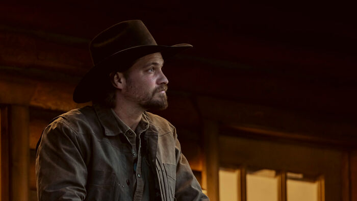 Man wearing a cowboy hat and brown jacket in a dimly lit rustic setting, related to Yellowstone fans and infamous location.