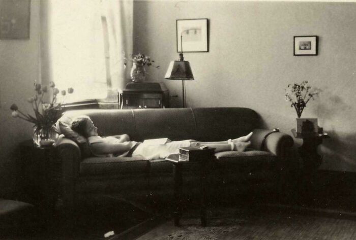 Candid old photos: A person relaxing on a couch in a cozy living room, showcasing life generations ago.
