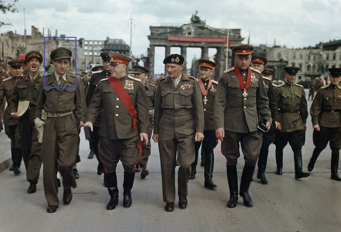 Group of military officers in vintage uniforms walking past a historic monument in an old photograph suggesting time travel mystery.