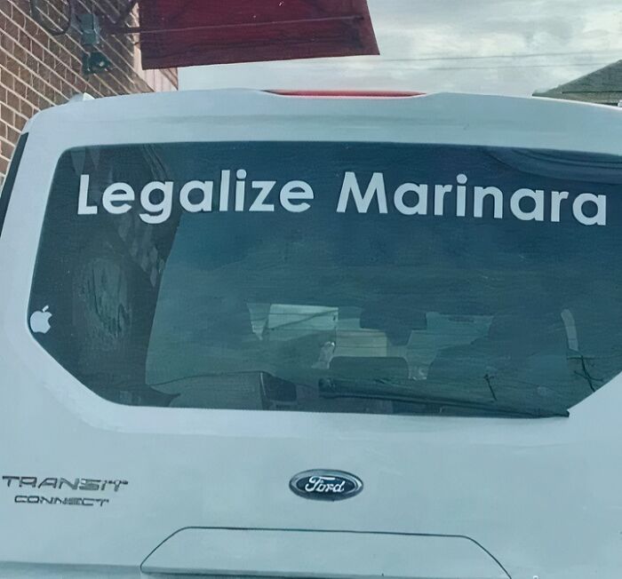 White Ford Transit Connect van with a humorous "Legalize Marinara" sign on the rear window, causing a double take.