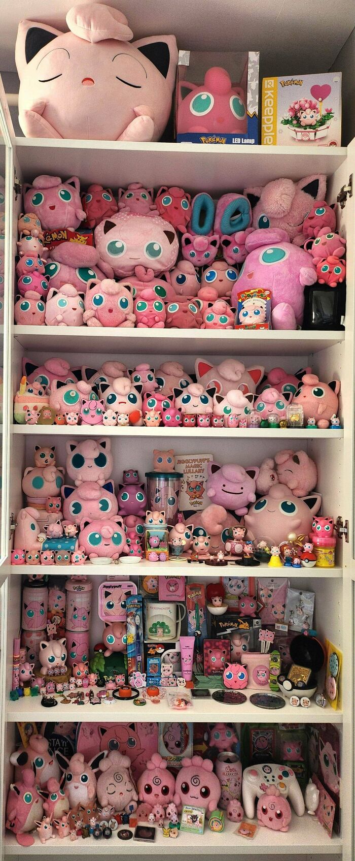 Shelf filled with a Pink Jigglypuff collection featuring plush toys, figurines, and various merchandise fans obsessively gathered.