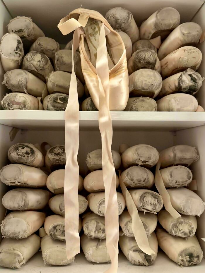 A collection of well-worn ballet pointe shoes stacked on shelves showing a ballet obsession collection.