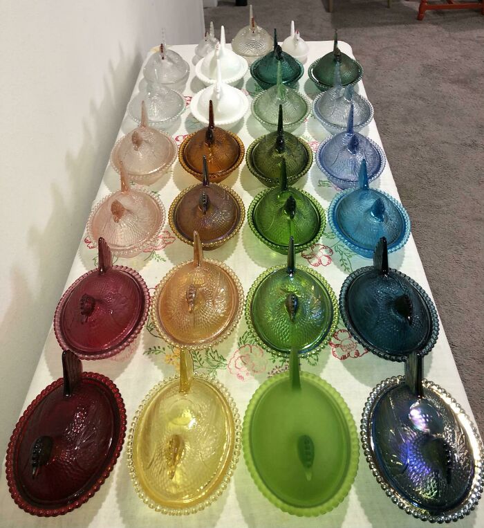 Colorful glass dish collection with lids arranged in rows on a table, showcasing an impressive obsession and collection.