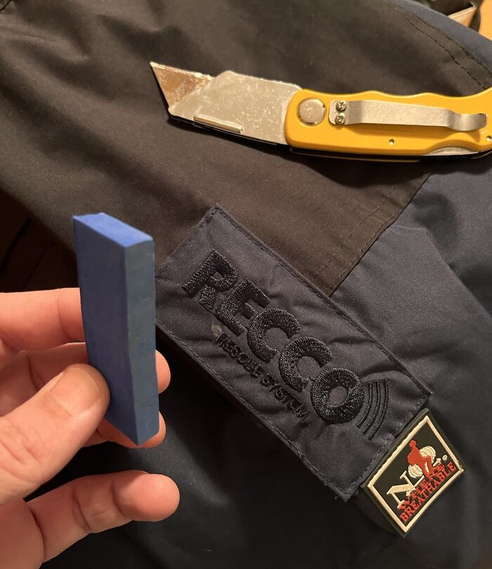 Hand holding a small block with a cutter and a jacket showing a RECCO rescue system patch in disappointing shopping fails.