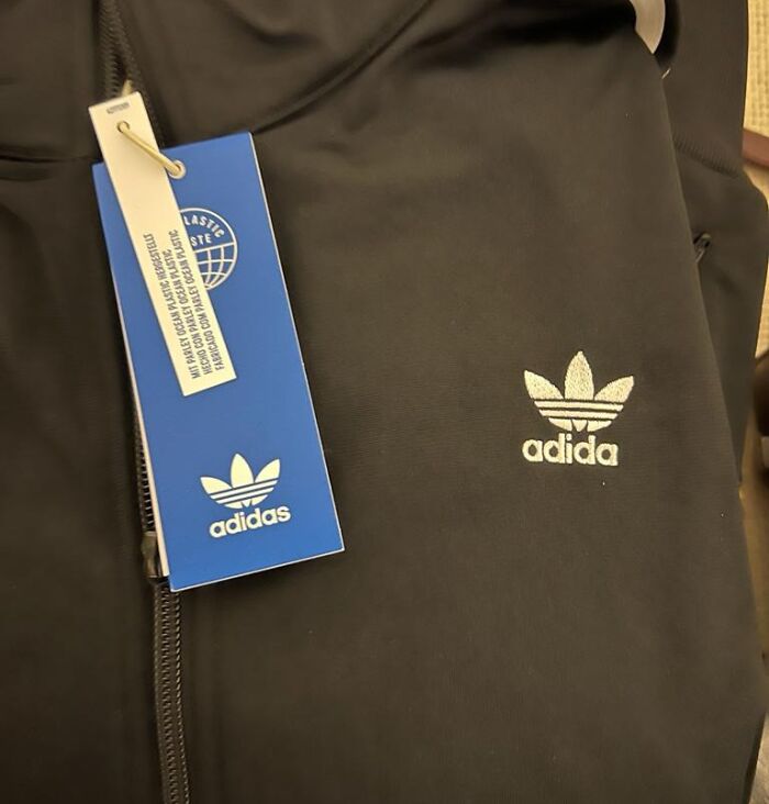 Black jacket with a fake Adidas logo and tag, illustrating a disappointing shopping fail causing trust issues.