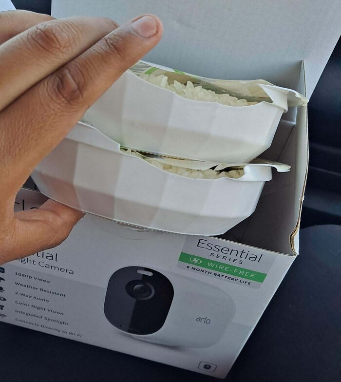 Hand holding containers of rice placed inside an empty security camera box showing disappointing shopping fails.
