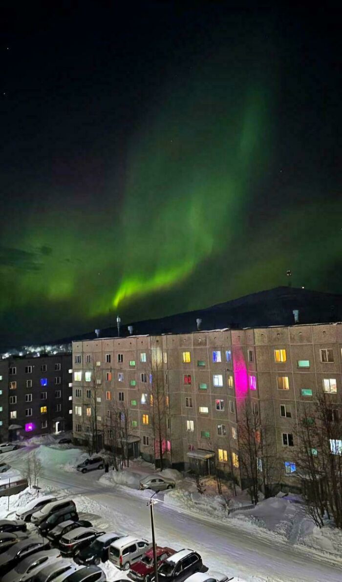 Urban hell scene of apartment building lit up at night beneath a glowing northern lights sky