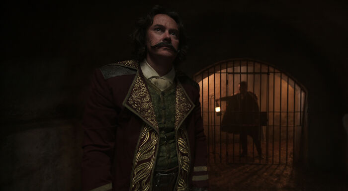 Man in ornate costume standing in dimly lit prison cell, hinting at One Piece Season 2 game-changing reveal scene.