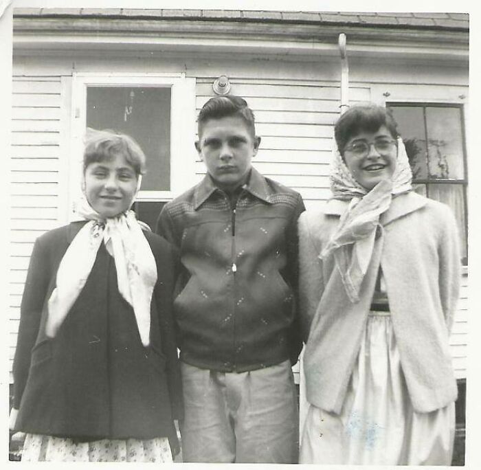 Vintage black and white photo of three teenagers posing outside a wooden house, evoking time travel mystery.