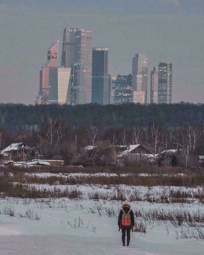 Urban hell showing lone figure walking in snowy field towards a distant city skyline of tall buildings