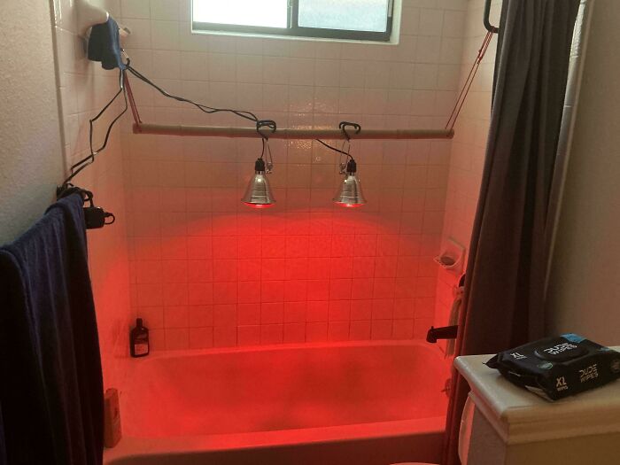 Bathtub with hanging red heat lamps rigged to a shower rod, demonstrating redneck engineering in a bathroom setup.