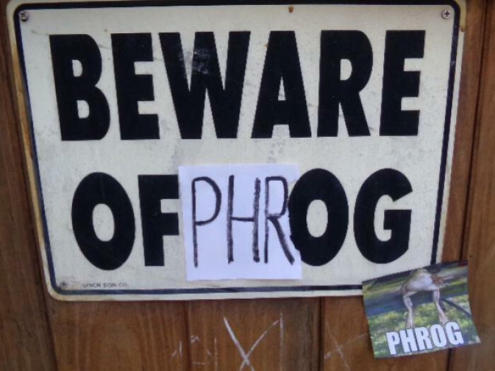 Beware sign altered with paper reading PHROG and a frog image sticker, showcasing mild vandalism humor.