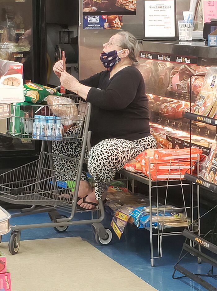 Woman wearing a mask sitting on a bench inside a store surrounded by bread, illustrating entitled Karen behavior.