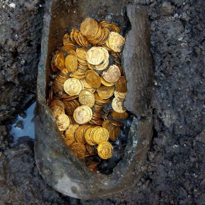 Almost perfectly preserved antique gold coins found in an ancient container buried in muddy soil revealing history secrets.