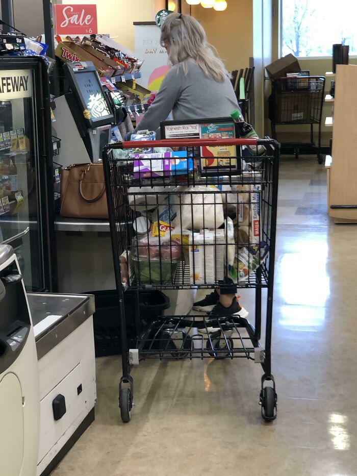 Woman at self-checkout with a full shopping cart in supermarket, illustrating entitled behavior often seen in Karens.