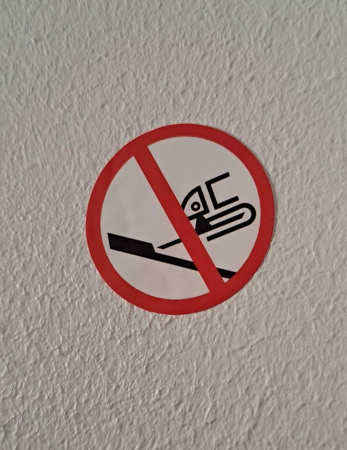 No smoking sign with a confusing design, showing a strange symbol inside a red circle on a textured white wall.