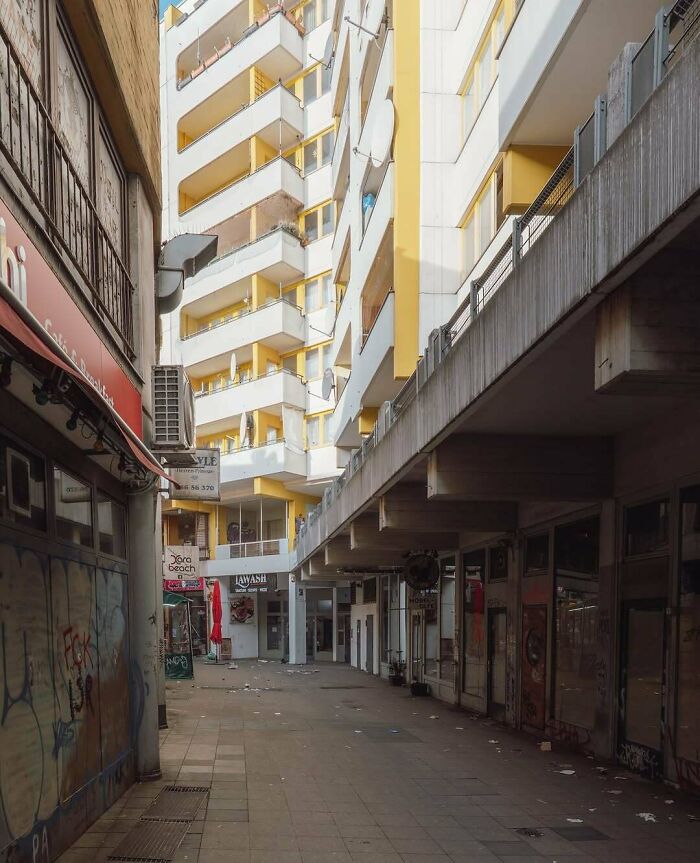 Empty eerie urban hell alley with graffiti, trash, and vacant shop fronts under bright daylight