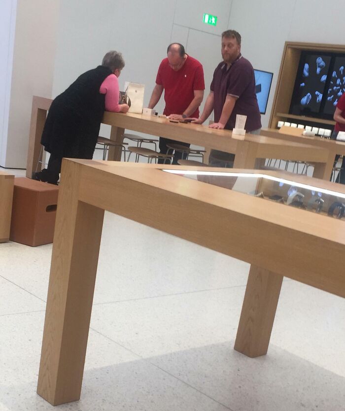 Three people interacting at a tech store counter with devices, illustrating entitled Karens missing sense of shame.