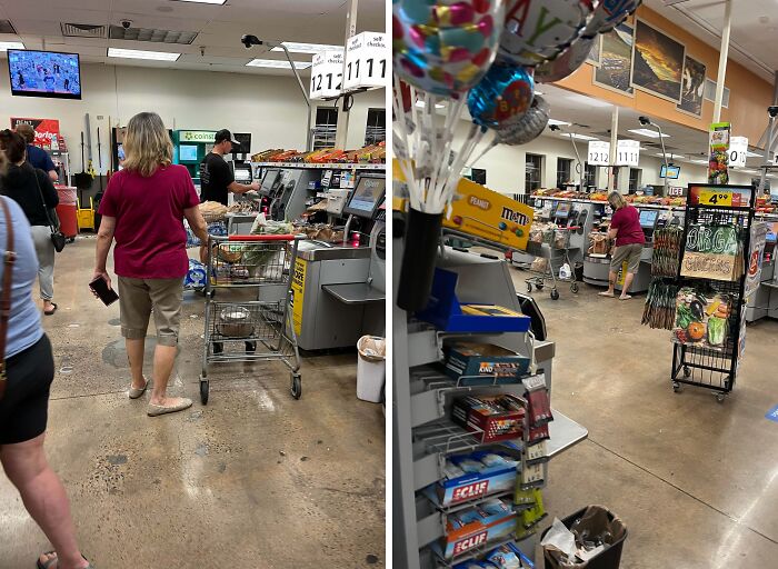 Woman in a red shirt pushing grocery cart in supermarket aisle with checkout lanes and snacks visible around.