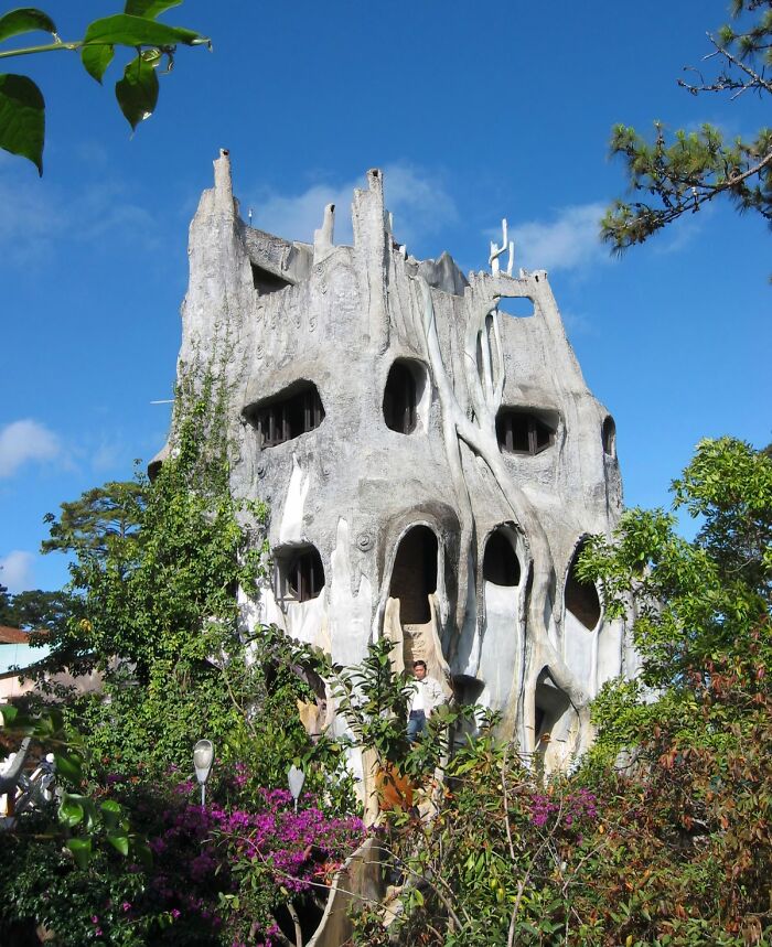 Unique unusual place with a surreal concrete structure surrounded by greenery and vibrant flowers under a blue sky.