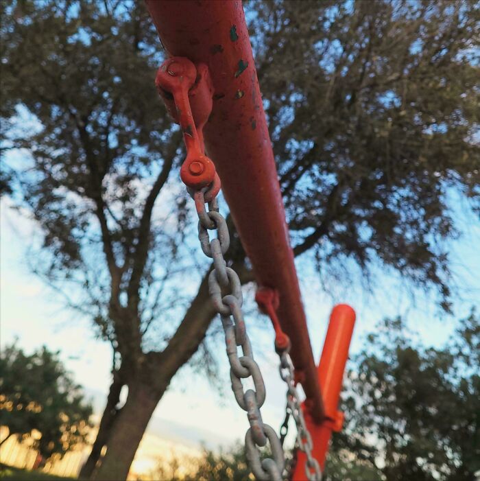 A close-up of a swing set chain and bar against a blurred sky and trees, representing wholesome outdoor play with a great dad.