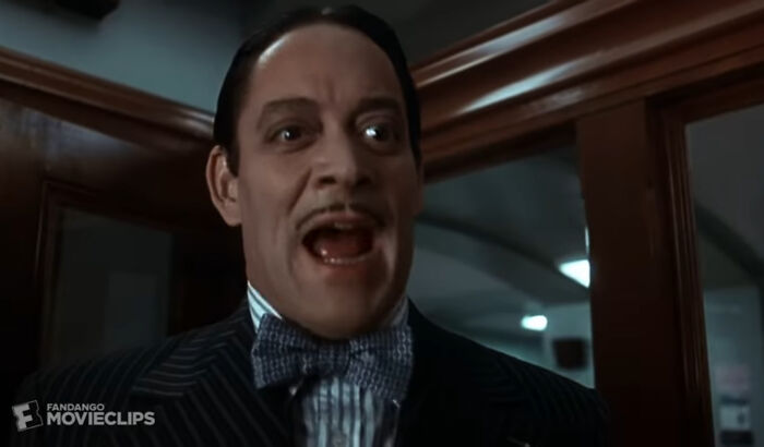 A man with a mustache and slicked-back hair, wearing a pinstripe suit and bow tie, with a surprised expression, highlighting nonsensical movie details.