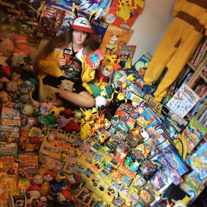 Person surrounded by an extensive Pokemon collection including cards, plush toys, and memorabilia in a colorful room.