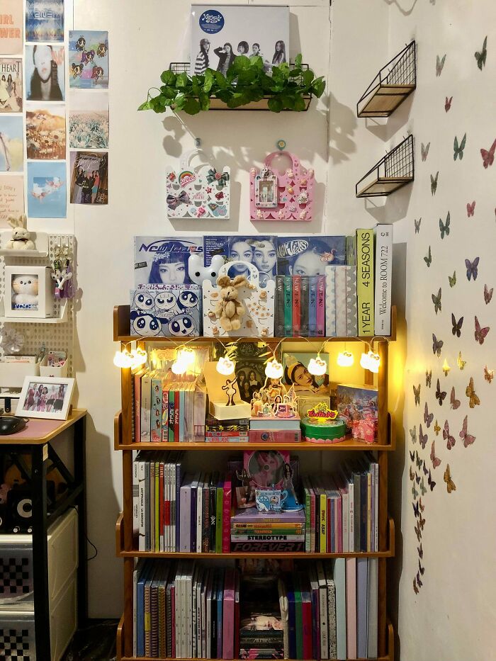 Collection of K-pop albums and memorabilia displayed on shelves with decorative lights and butterfly wall stickers.