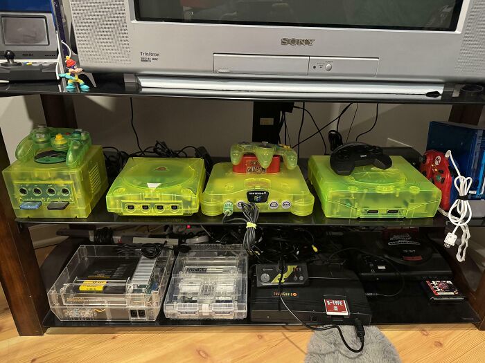 Collection of neon green translucent retro gaming consoles and accessories neatly displayed on shelves.
