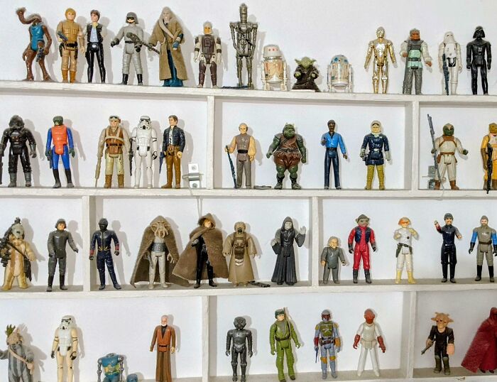 Collection of Star Wars action figures neatly displayed on white shelves, showcasing a popular obsession turned collection.